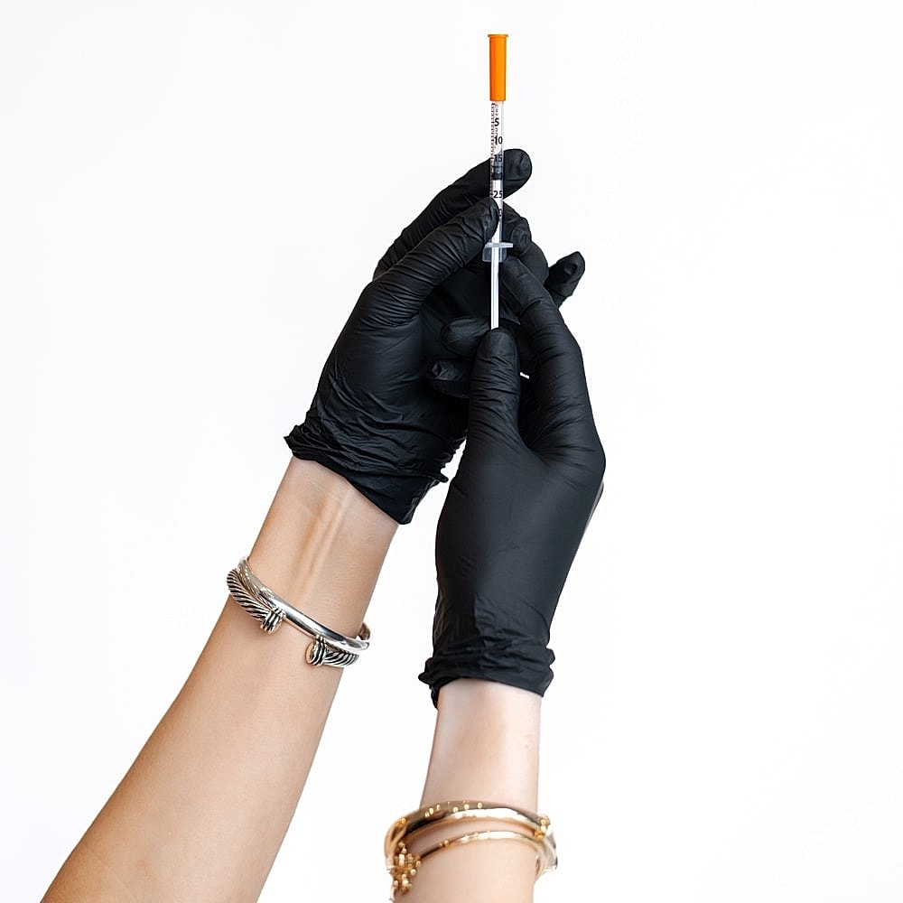 Hands in black gloves holding a syringe.