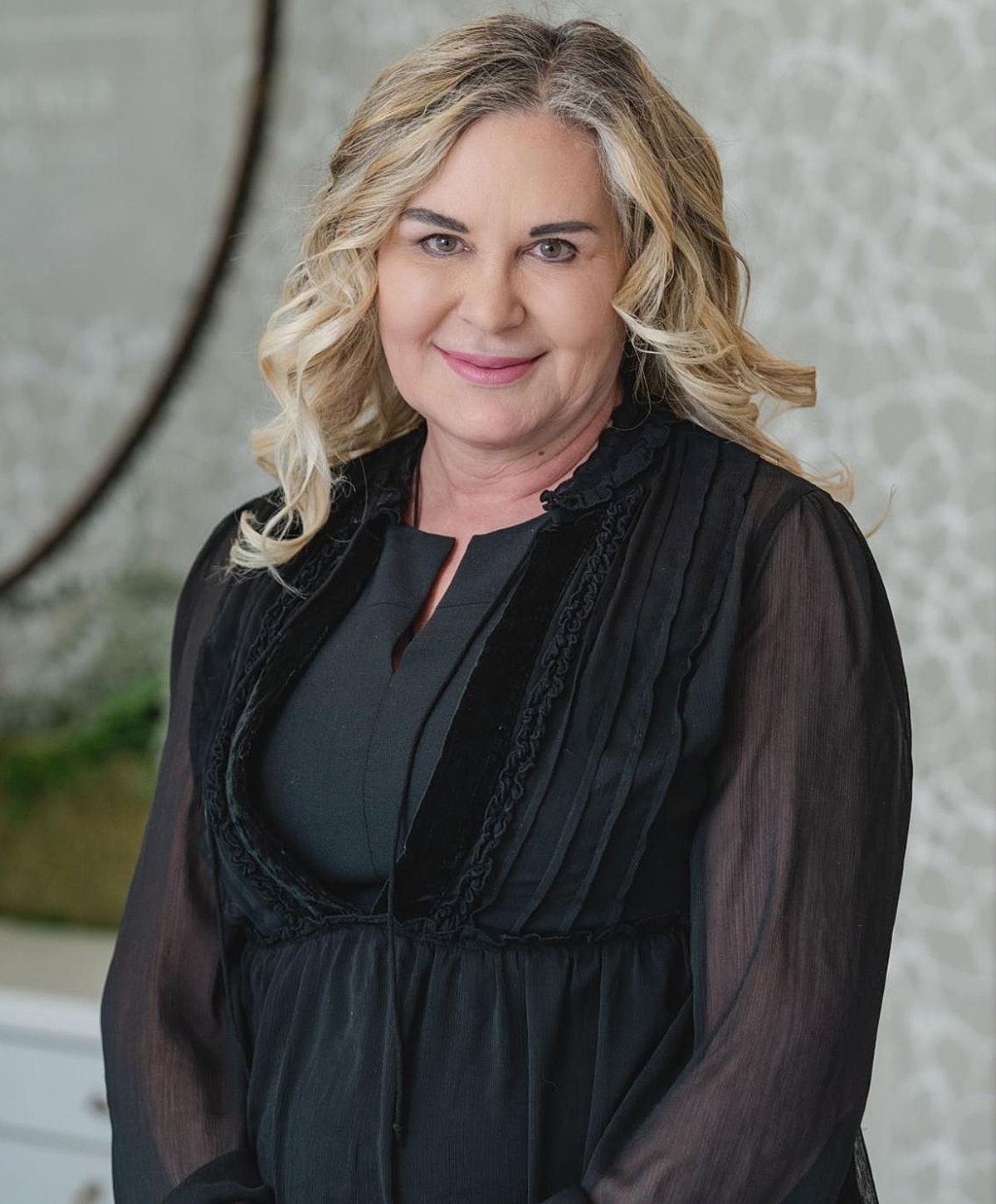 Smiling woman with long blonde hair in black attire.